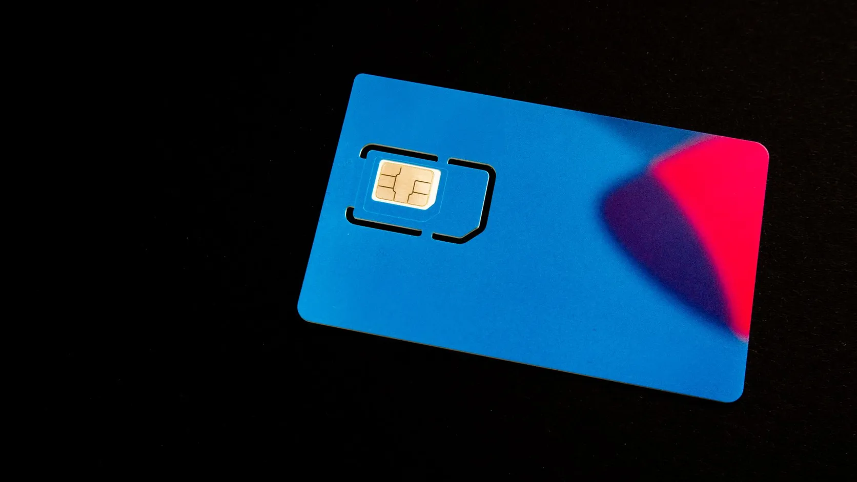 Carte SIM bleue avec sa puce dorée prédécoupée, posée sur un fond noir avec un reflet rouge et violet