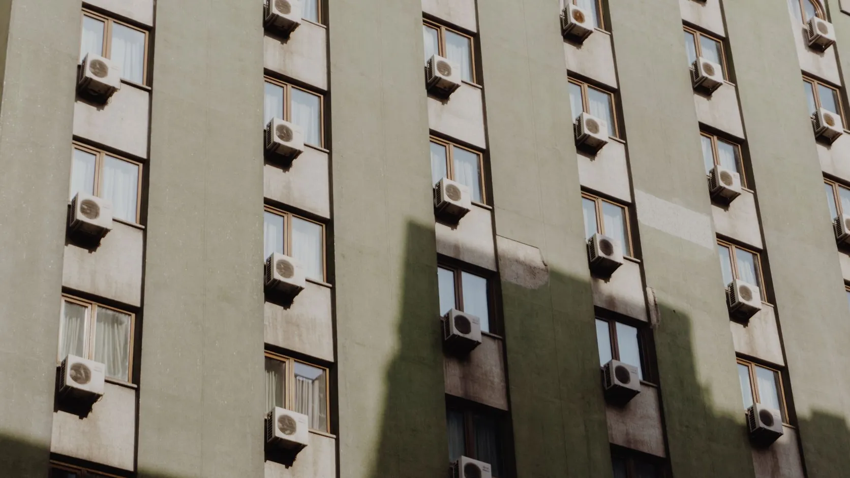 Façade d'immeuble vert-gris dont chaque fenêtre porte un bloc de climatisation extérieur