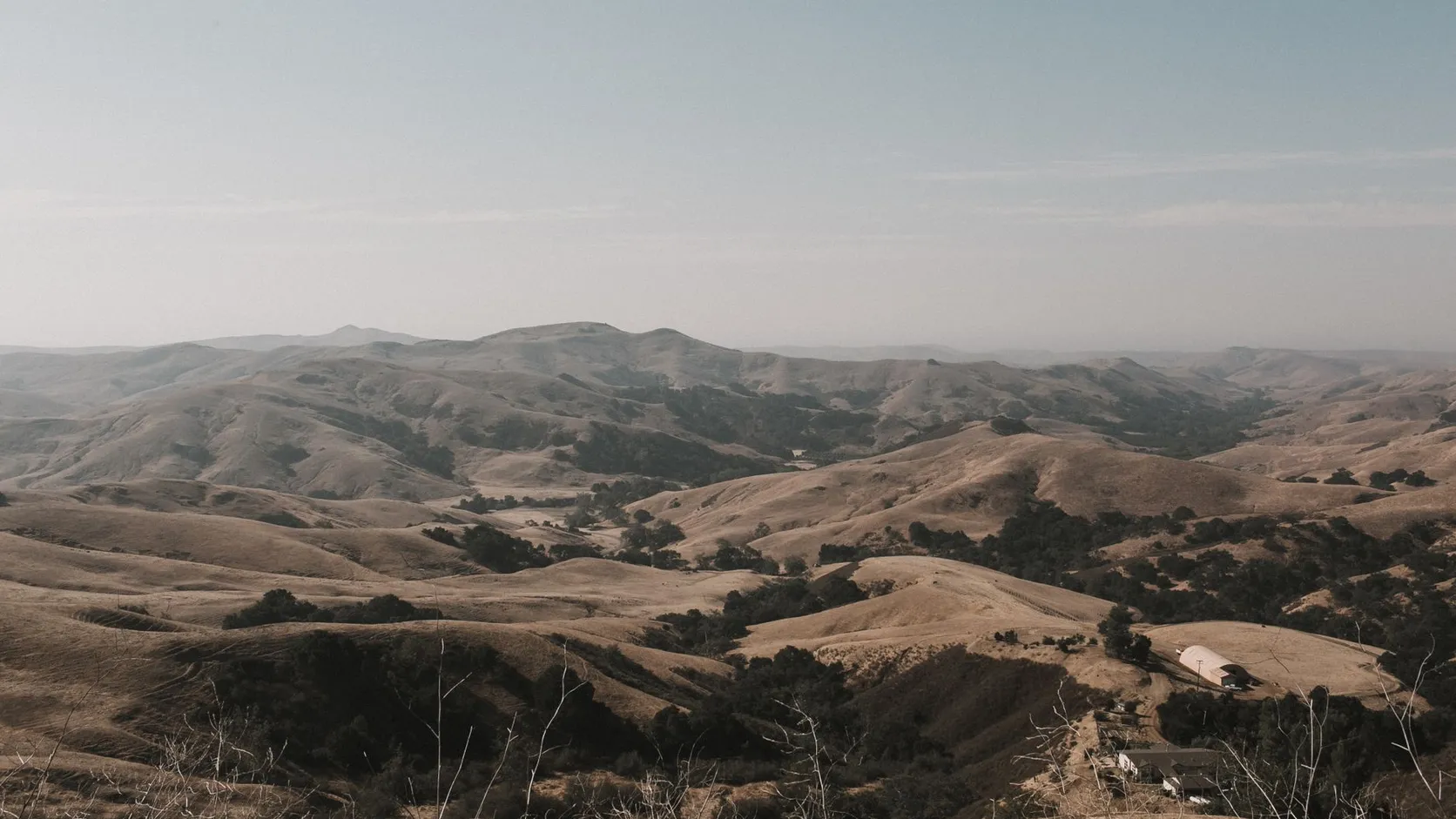 Collines sèches et dorées de Californie piquées de chênes sombres, avec quelques bâtiments de ferme au premier plan