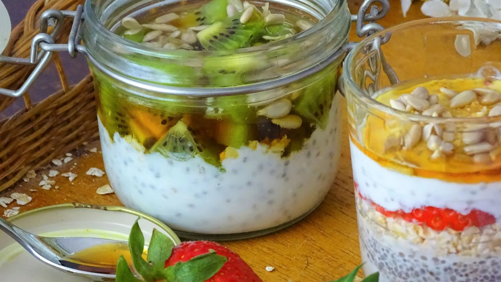 Bocaux en verre de pudding aux graines de chia garnis de kiwi, de graines de tournesol et de miel, avec une fraise au premier plan