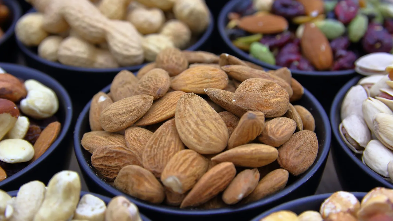 Bols noirs remplis d'amandes, de cacahuètes en coque, de pistaches et d'un mélange de fruits secs aux canneberges