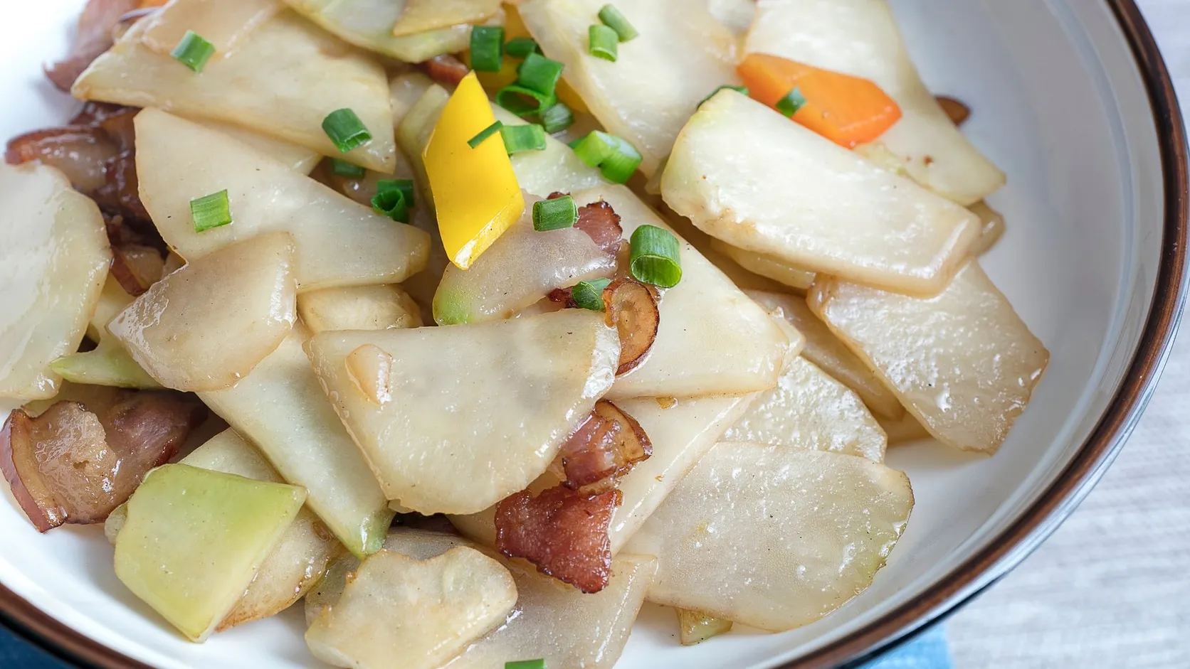 Lamelles de radis blanc sautées avec des lardons, du poivron jaune, de la carotte et de la ciboule dans une assiette creuse