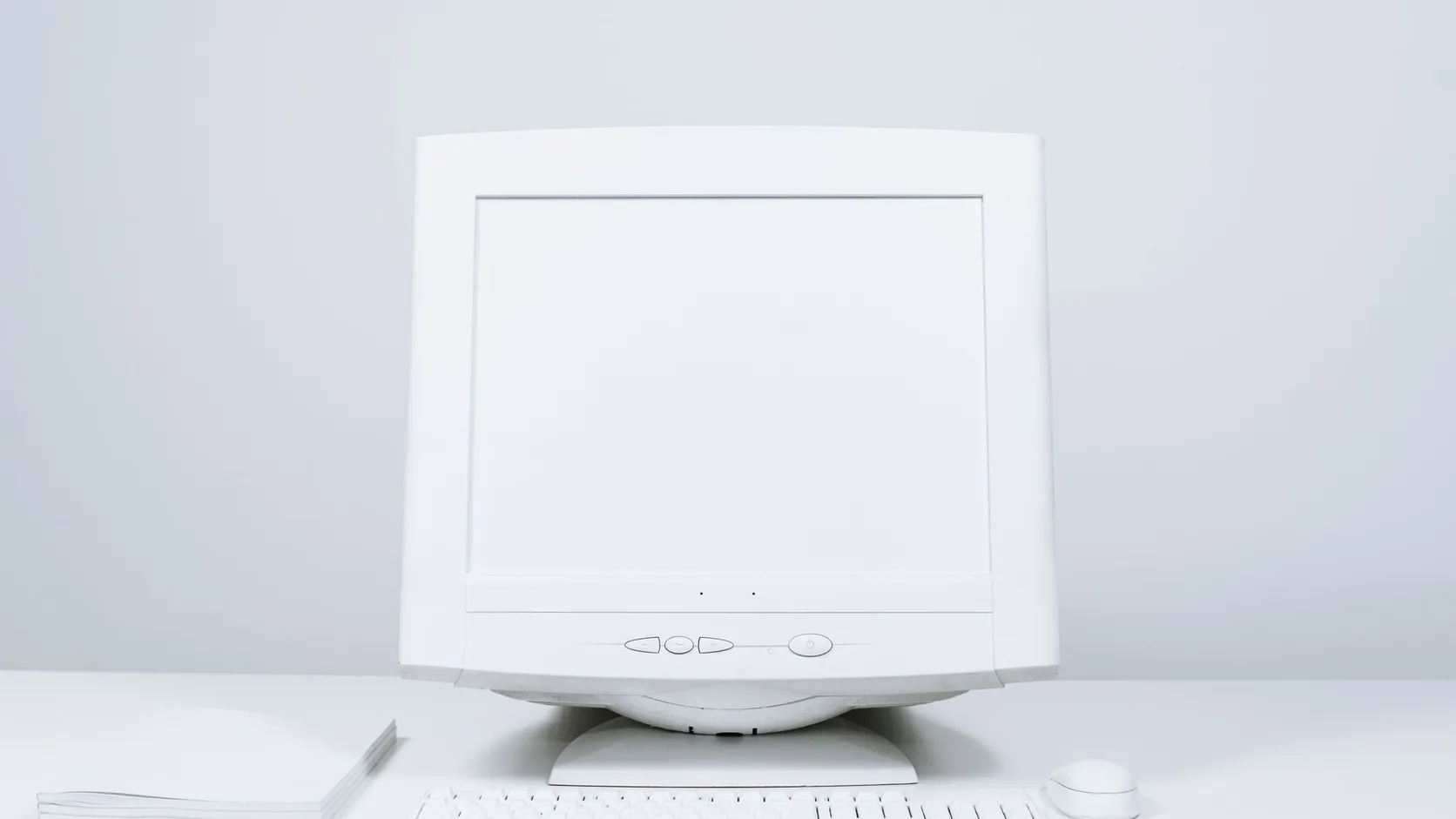 Ancien moniteur d'ordinateur blanc à écran vide, posé sur un bureau blanc avec clavier et souris