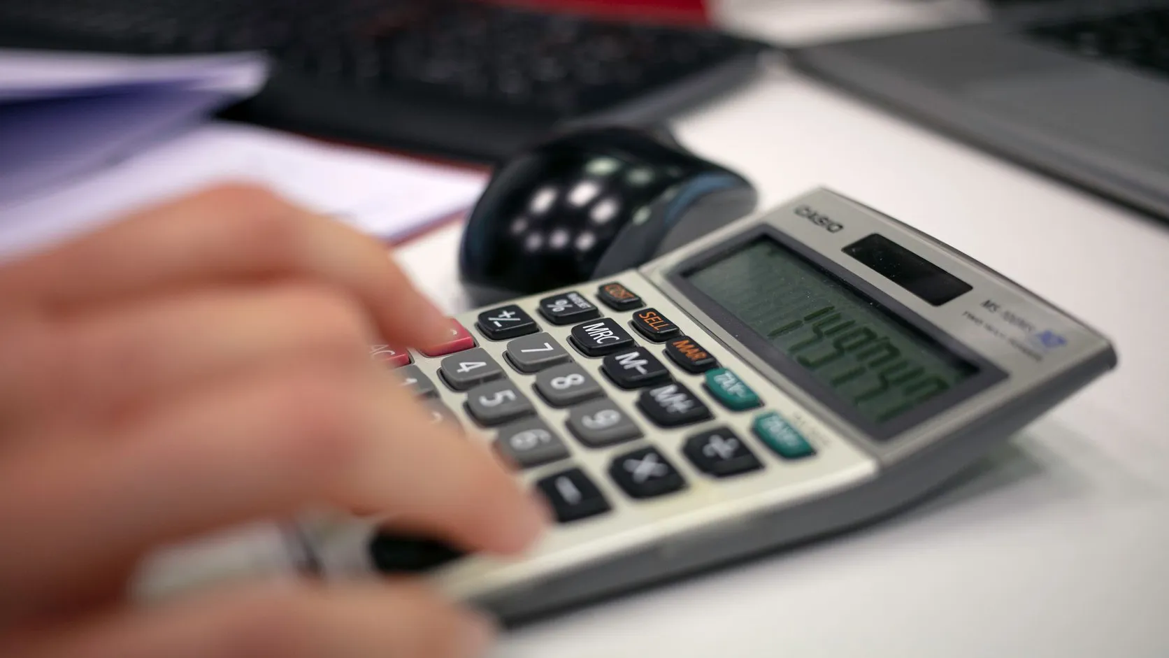 Main tapant des chiffres sur une calculatrice de bureau posée à côté d'une souris d'ordinateur